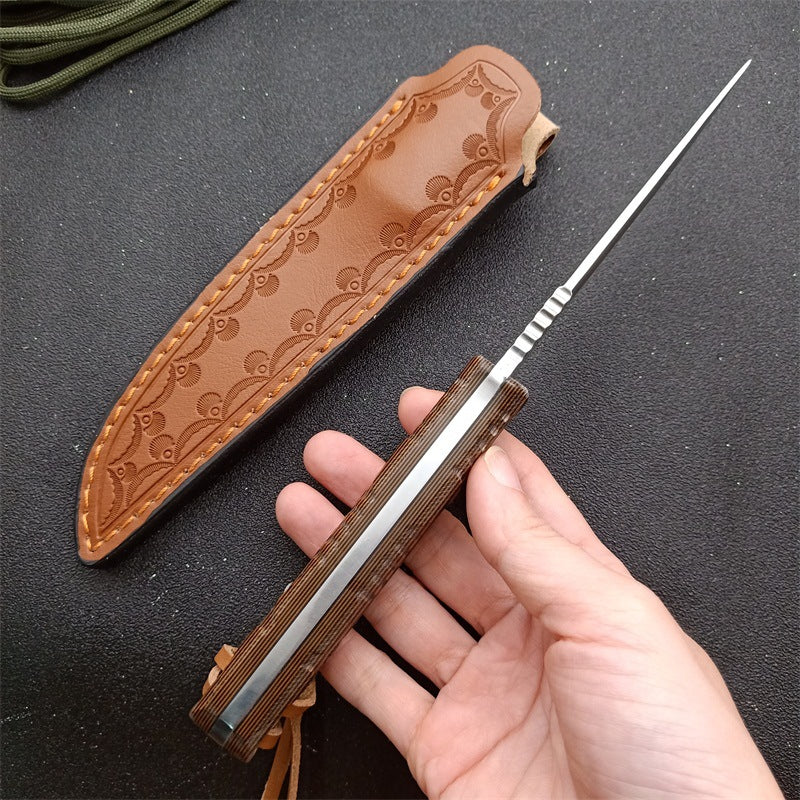 Hand holding a fixed blade knife with wooden handle and a leather sheath on black surface