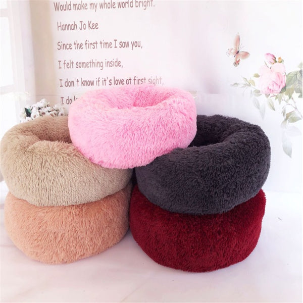 Stack of soft plush round pet beds in pink, beige, gray, red, and peach for cats and dogs