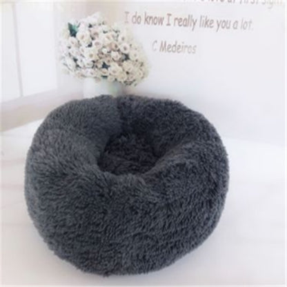 Gray plush round pet bed on white surface with white flower bouquet in vase