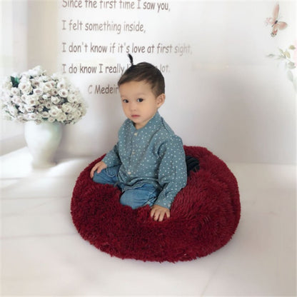 Child sitting on a plush, round, red pet bed in a bright room with flower vase and wall text