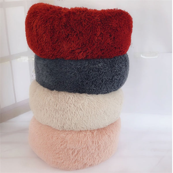 Stack of four round plush pet beds in red, dark gray, beige, and light pink colors on white surface