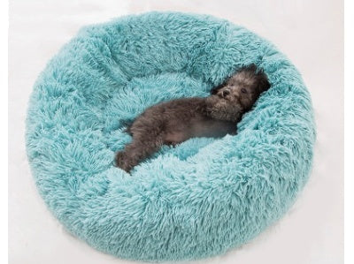 Small dark gray dog lying on light blue fluffy round plush pet bed on white background