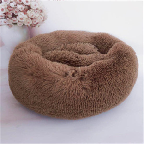 soft round brown plush pet bed with raised edges on white surface near vase with pink flowers