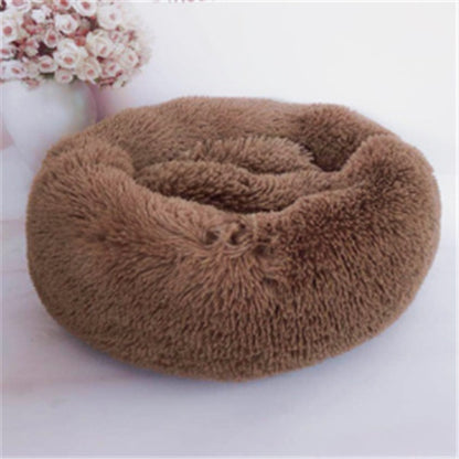 soft round brown plush pet bed with raised edges on white surface near vase with pink flowers