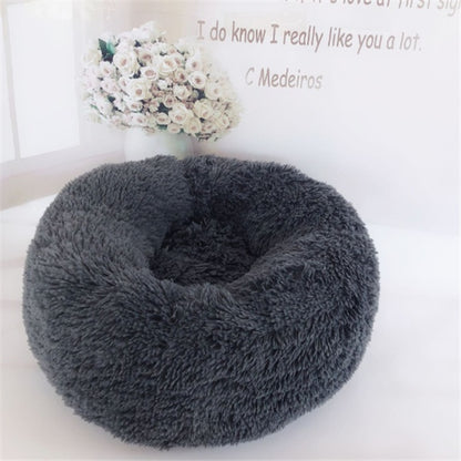 Round fluffy dark gray plush pet bed for cats and dogs on white surface with white roses bouquet