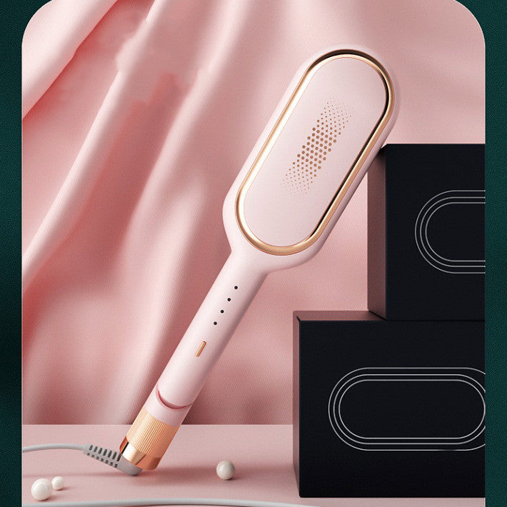 Pink and rose gold electric hair styling brush on a pink surface with black boxes and fabric backdrop