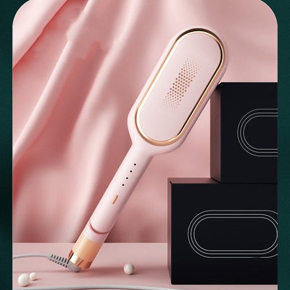Pink and rose gold electric hair styling brush on a pink surface with black boxes and fabric backdrop