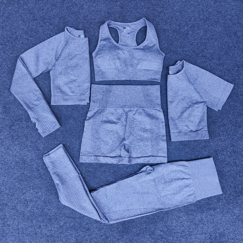 Five-piece blue seamless nylon athleisure set including sports bra, long-sleeve crop top, short-sleeve top, shorts, and leggings on carpet