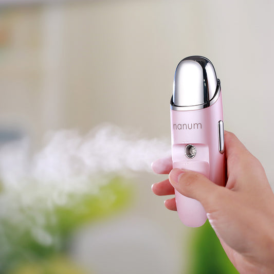 Hand holding pink portable nanum facial mist sprayer releasing fine moisturizing mist