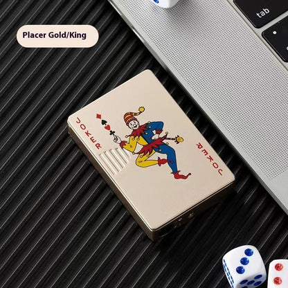 Gold zinc alloy lighter with colorful joker card design beside laptop and dice on black surface