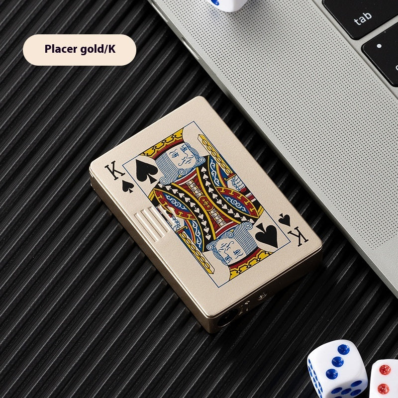 Gold zinc alloy lighter designed like King of Spades poker card next to laptop and dice on black surface
