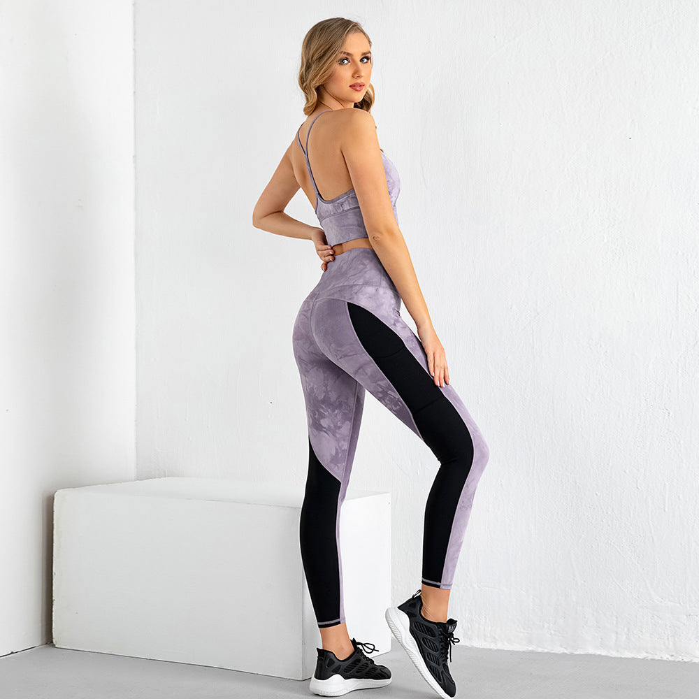 Woman wearing purple tie-dye two-piece gym suit with sleeveless crop top and leggings with black panels, black sneakers