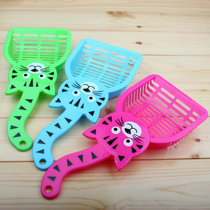 Colorful plastic cat litter scoops in green, blue, and pink with cartoon cat faces on wooden surface