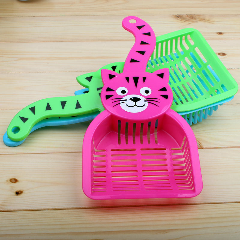 Pink and green plastic cat litter scoops with cat face and striped tail design on wooden surface