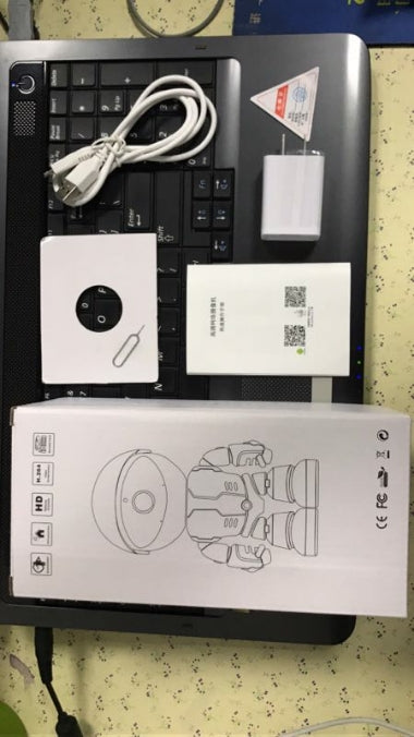 WiFi IP camera kit with USB cable, power adapter, instruction manual, SIM card tool, and packaging on laptop keyboard