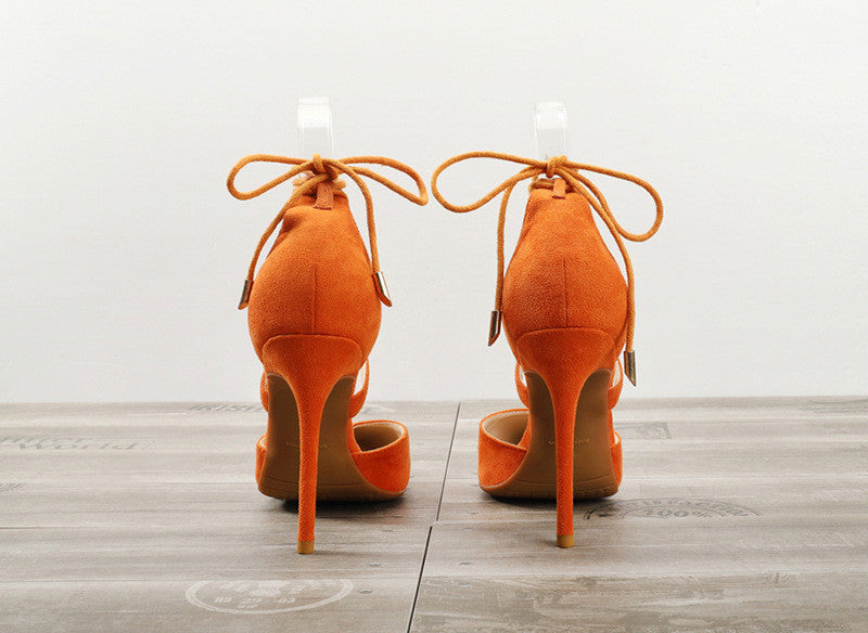 Pair of orange suede women's high heel sandals with ankle straps on wooden floor