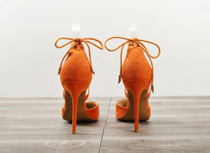 Pair of orange suede women's high heel sandals with ankle straps on wooden floor