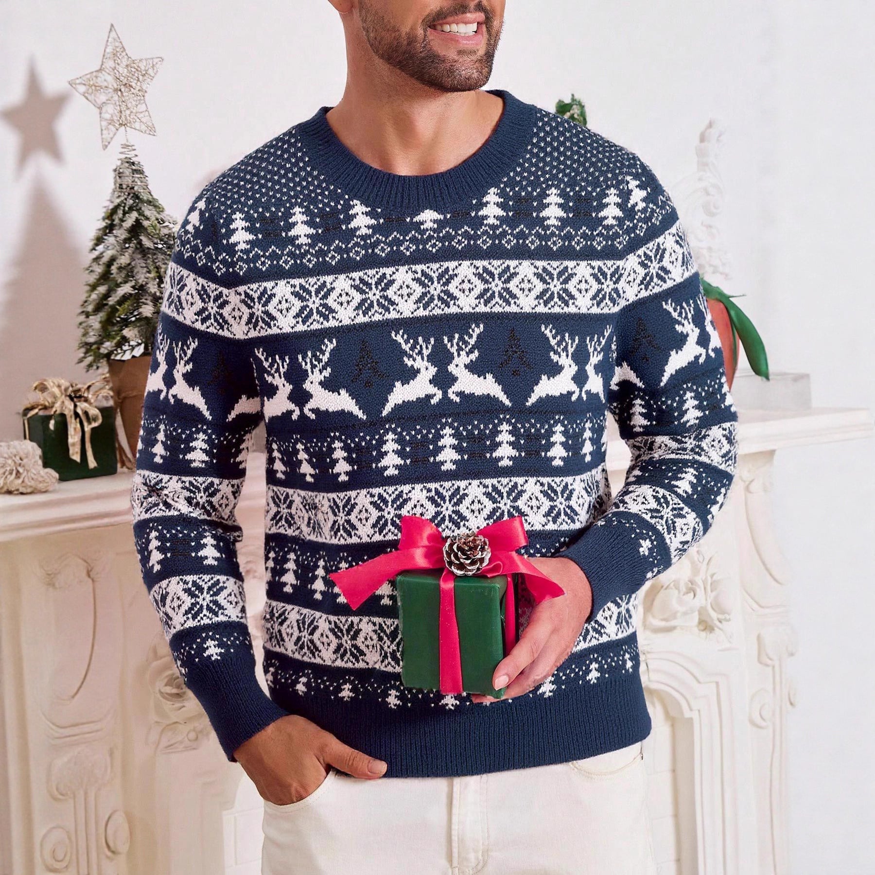 Man wearing blue and white Christmas sweater with reindeer and tree patterns holding green gift box with red ribbon