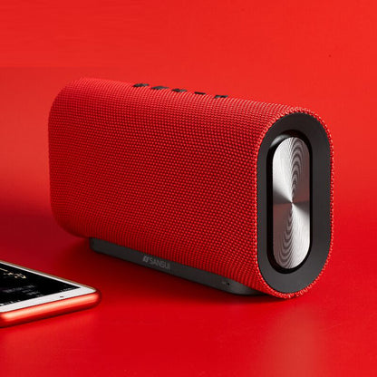 Red Sansui wireless Bluetooth portable speaker with subwoofer on red surface next to smartphone