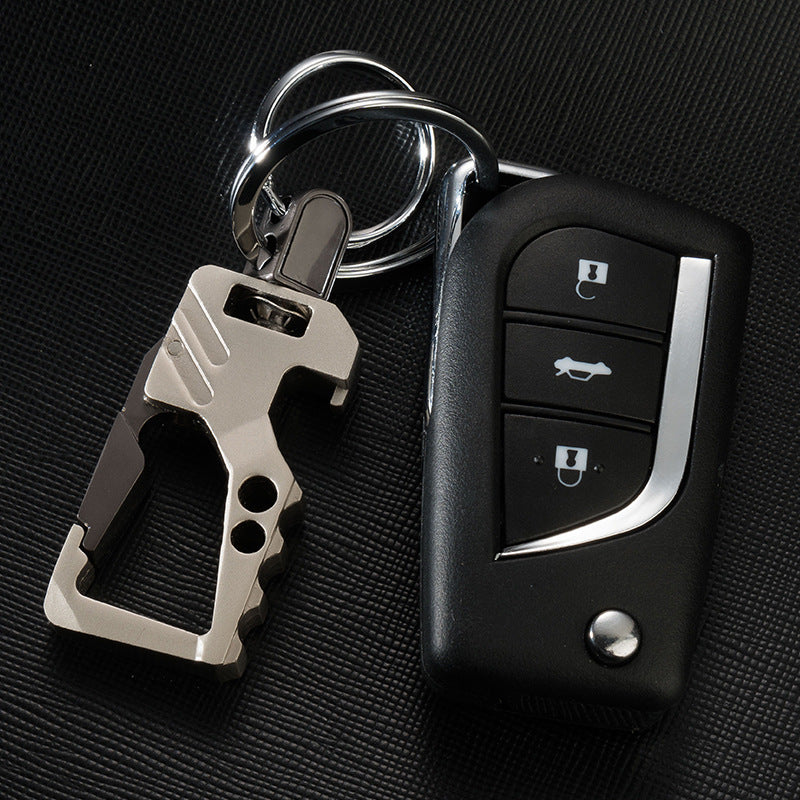 Men's leather car key chain pendant with a sandy gold multi-tool and black car remote on black textured surface