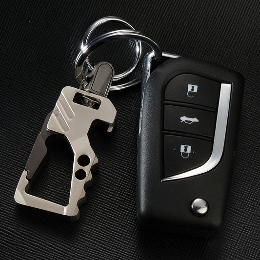 Men's leather car key chain pendant with a sandy gold multi-tool and black car remote on black textured surface