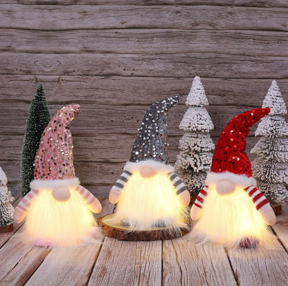 Three glowing Christmas gnome decorations with sequin hats in pink, gray, and red, surrounded by snowy miniature trees