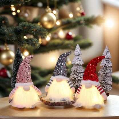 Three glowing Christmas gnome decorations with sequin hats and snowy tree ornaments on wooden surface