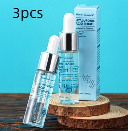 Three Vibrant Glamour hyaluronic acid serum bottles with droppers and box on wooden slices against blue background