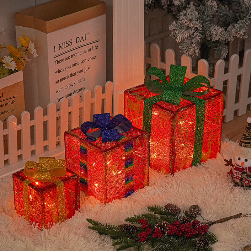 Three decorative red Christmas gift boxes with warm LED lights and glittery bows in cozy holiday setting