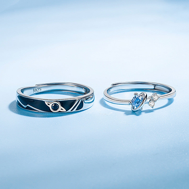 Two sterling silver rings on light blue surface, one with planet design and black stone, one with blue gem and clear crystals