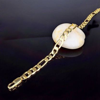 Gold-tone Figaro chain bracelet with copper plating resting on a white stone over black surface