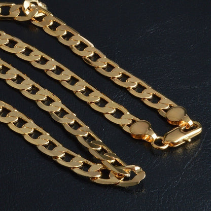 Close-up of shiny gold figaro chain bracelet with a box clasp on black textured surface