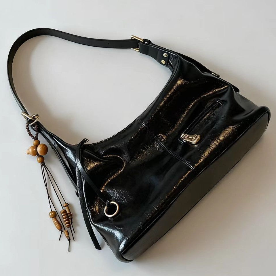 Shiny black leather shoulder bag with wooden bead tassel and zipper pocket on white background