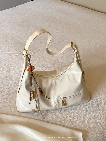 Cream white PU leather shoulder bag with tassel and wooden bead decoration on beige fabric surface