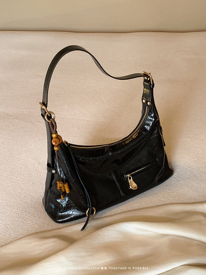 Black PU leather shoulder bag with front zipper pocket and wooden bead tassel on beige surface