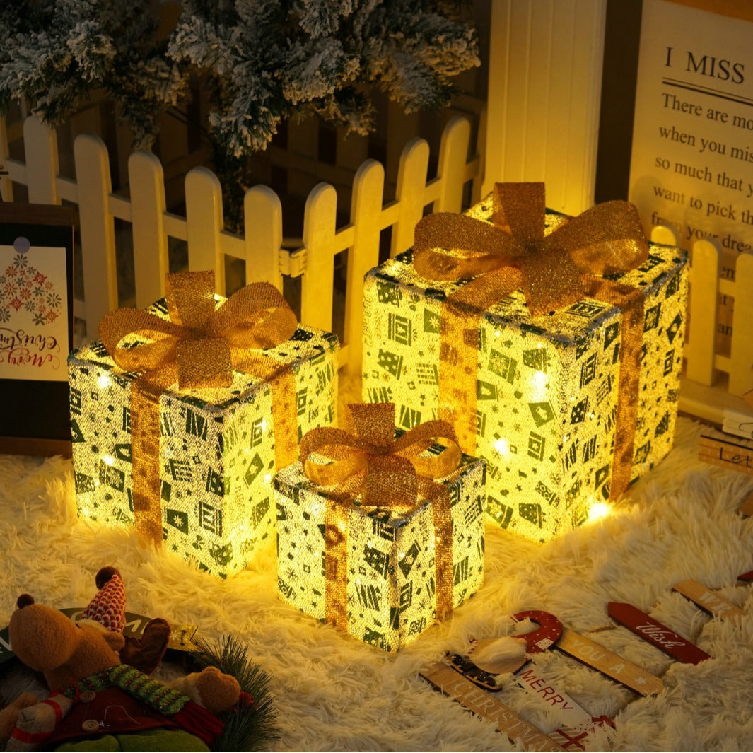 Glowing three-color Christmas gift box lights with golden ribbons on fluffy white surface, holiday decor
