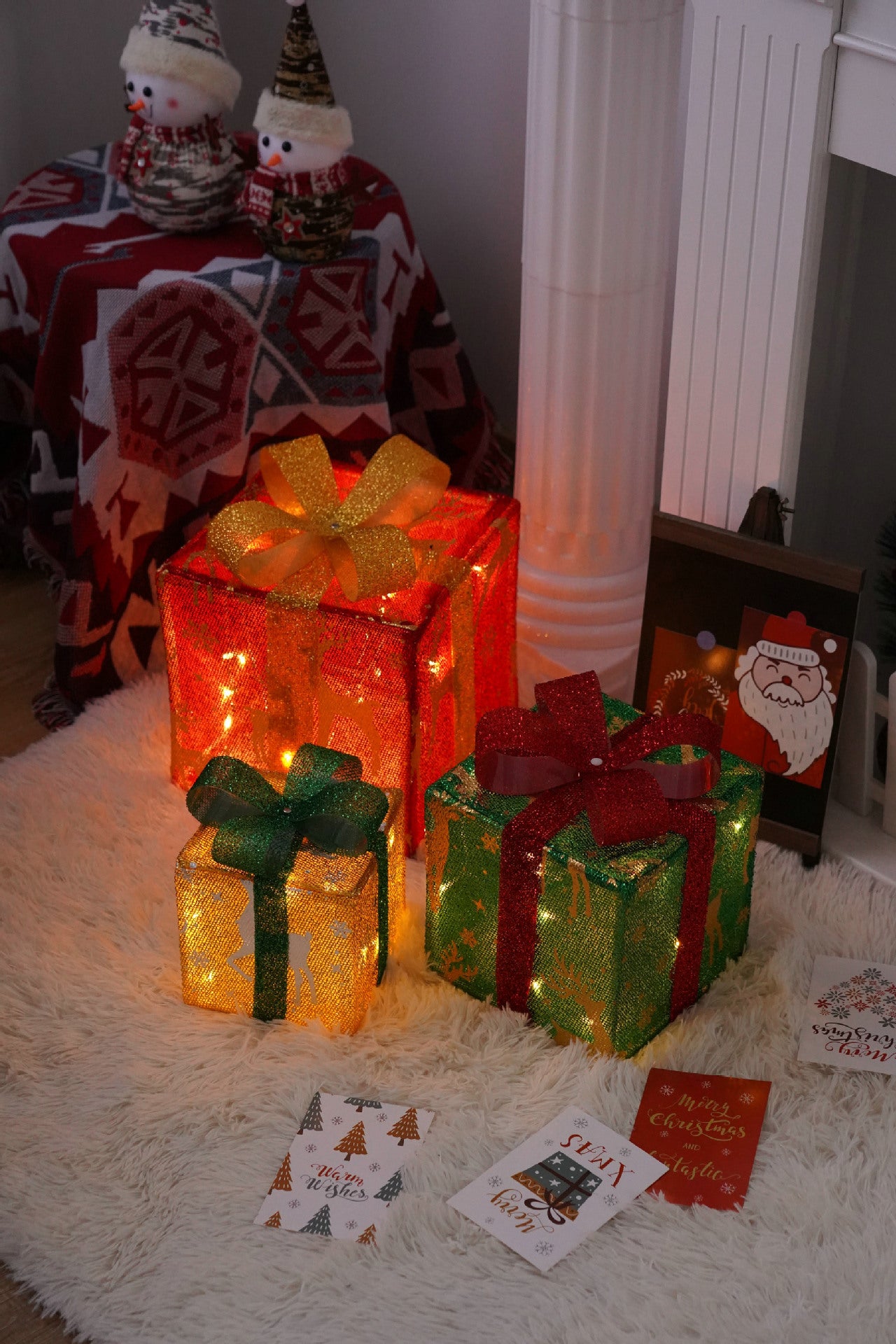 Three glowing Christmas gift boxes with golden, green, and red ribbons on a white furry rug, holiday cards nearby