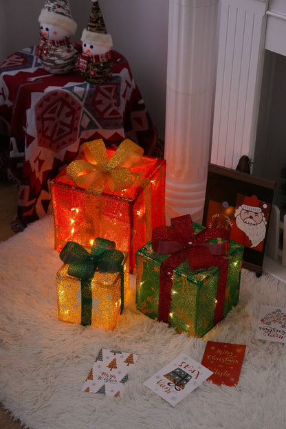 Three glowing Christmas gift boxes with golden, green, and red ribbons on a white furry rug, holiday cards nearby