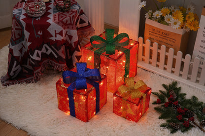 Three glowing red Christmas gift boxes with blue, green, and gold bows on a white rug next to festive decor