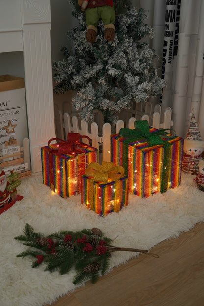 Three glowing rainbow-striped Christmas gift boxes with glitter bows under a snow-frosted tree on a white rug