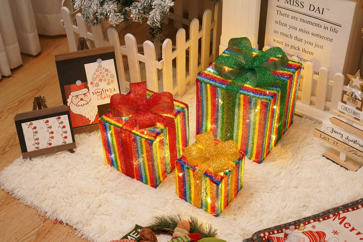 Three colorful striped Christmas gift boxes with red, green, and gold bows, decorated with lights, on a white rug