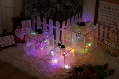 Three white mesh Christmas gift boxes with multicolor fairy lights and pinecone decorations on fuzzy rug