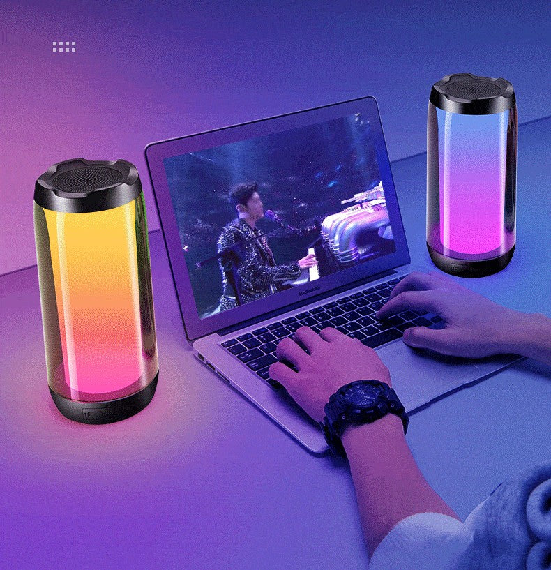 Colorful ambient light Bluetooth speakers beside laptop showing a live music performance, hands on keyboard