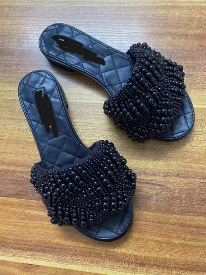 Black quilted flat sandals with thick straps covered in black beads on wooden floor