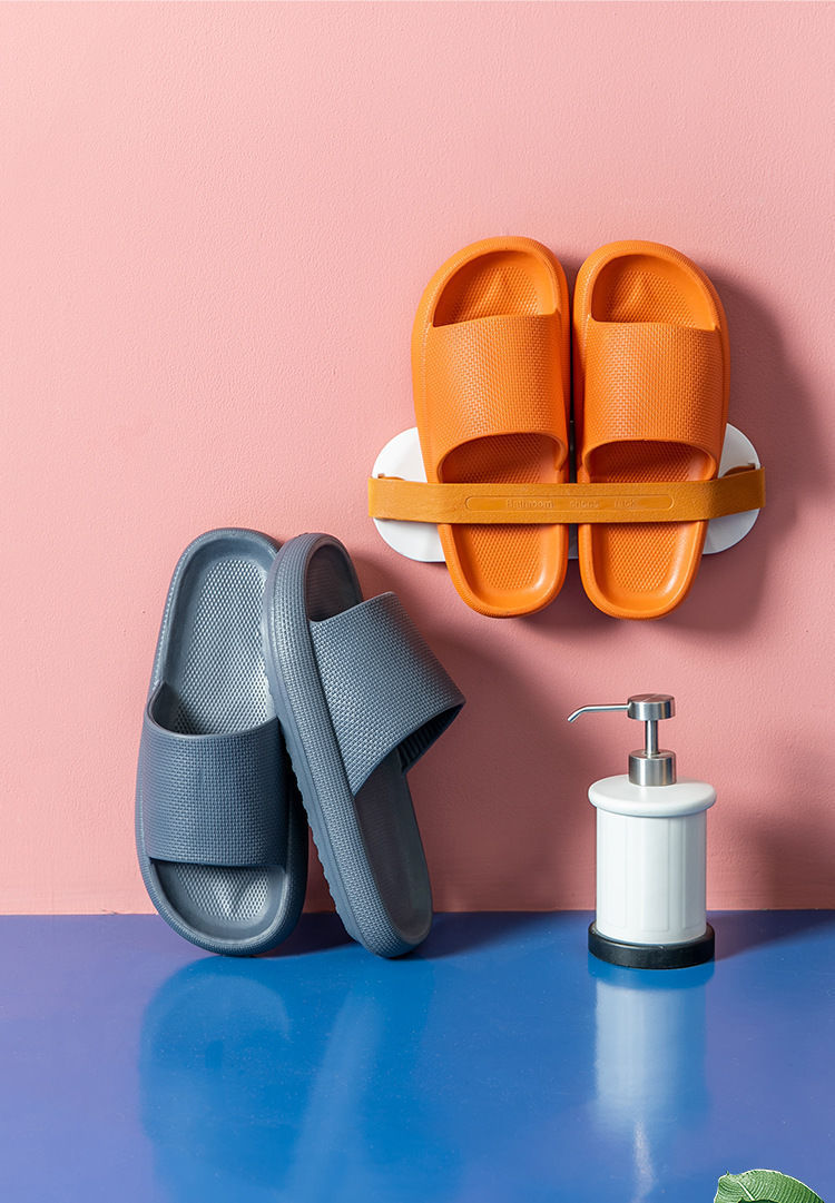Orange and gray EVA cushioned comfort slides displayed against pink wall and blue surface with white soap dispenser