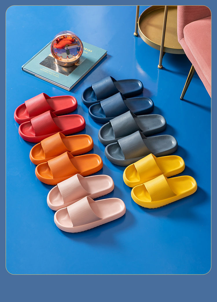 Colorful cushioned EVA slide sandals in red, orange, pink, blue, gray, and yellow on blue floor beside pink sofa