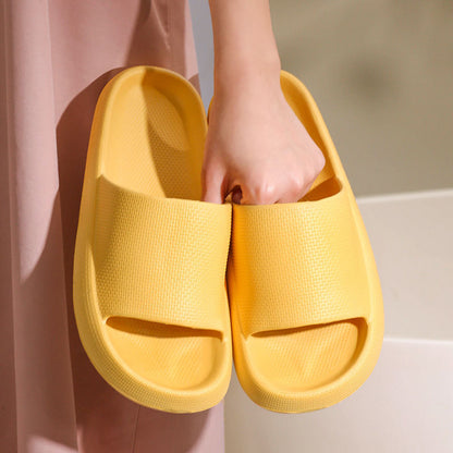 Hand holding bright yellow cushioned EVA slide sandals with thick sole, textured slip-on slippers
