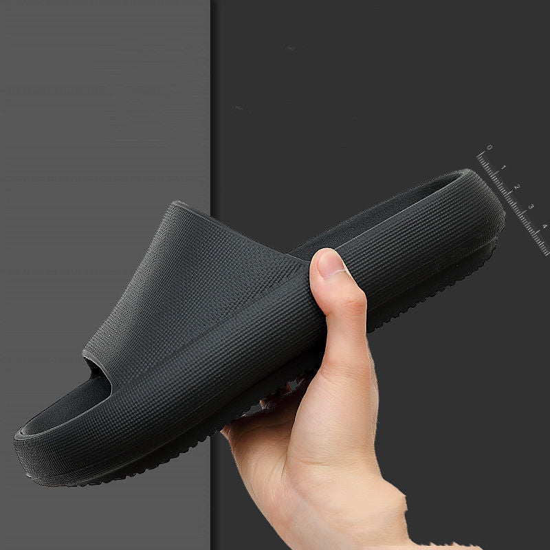 Hand holding a black EVA slide sandal with textured thick sole and cushioned footbed on dark background