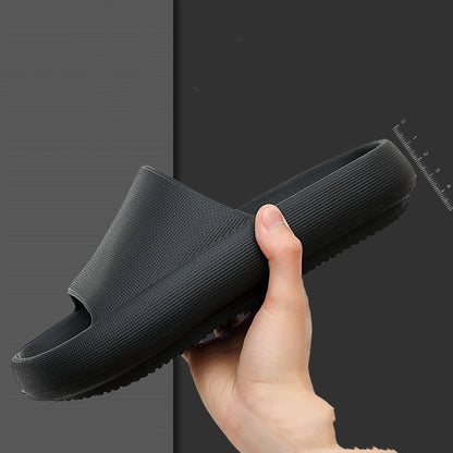 Hand holding a black EVA slide sandal with textured thick sole and cushioned footbed on dark background
