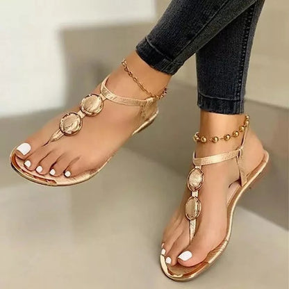 Women's gold flat sandals with metal buckle, worn with black jeans and gold anklets